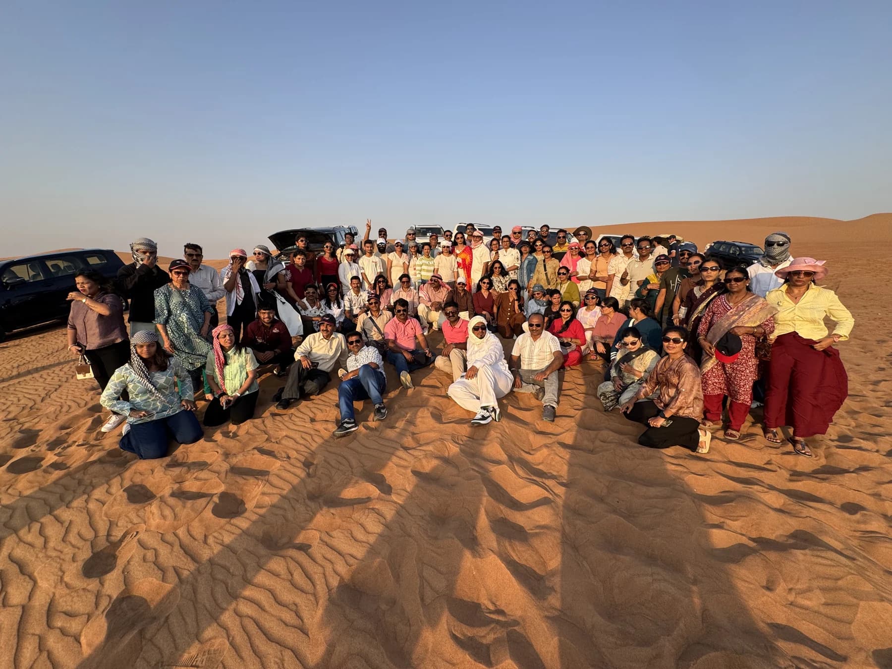 Guests posing on Lahbab dunes with several vehicles behind them