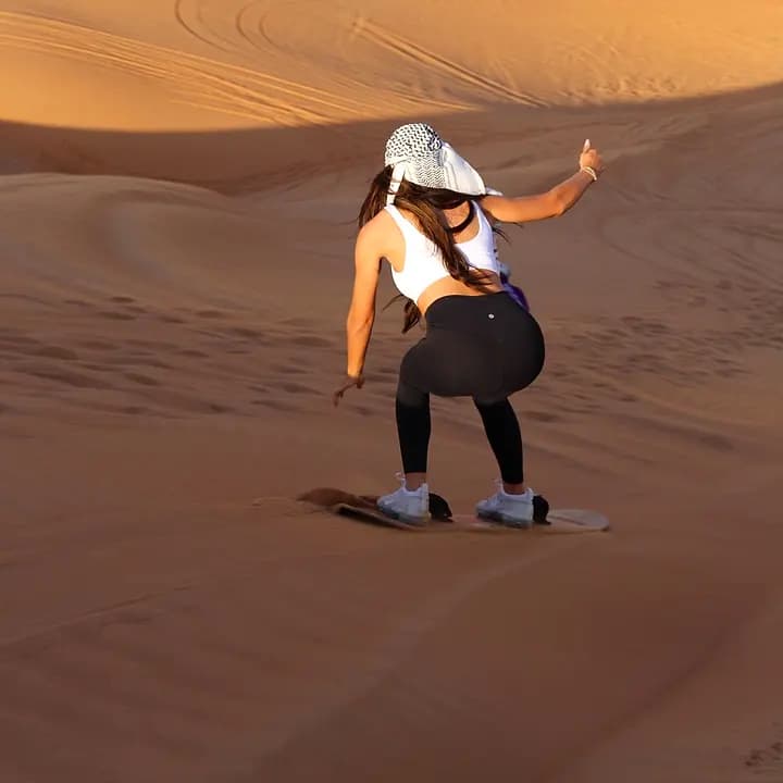 A guest sandboarding down a red dune at Lahbab